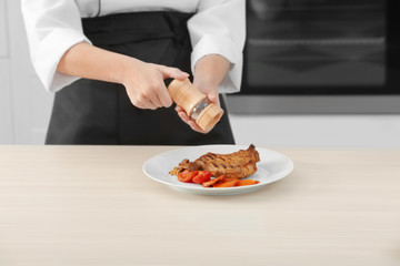 Female chef hands with pepper mill over plate with meat