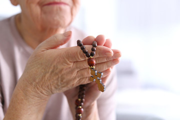 Elderly woman with rosary beads at home, closeup