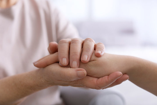 Hands of elderly mother and daughter on blurred background, closeup