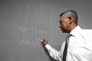 Confident Indian teacher writing math formulas on blackboard