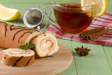 Biscuit swiss roll with a cup of tea on  green wooden background