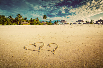 Two hearts drawn on sand of a tropical beach. Vintage