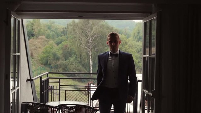 Young attractive groom man coming into hotel room from balcony, slowmotion 120 FPS