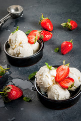 Vanilla ice cream in a classic ice-cream bowls with strawberries and mint, ice cream spoon on dark gray stone table