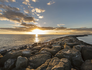 Hawaiian Sunset over a rock barrier