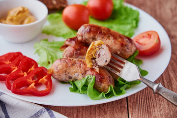 Grilled sausages with vegetables on a wooden background.