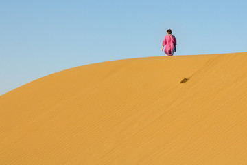 Fototapeta na wymiar Woman walking on Sand dunes in the Maranjab desert, near Kashan, Iran