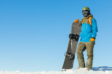 Young snowboarder in helmet at the very top of a mountain with beautiful sky on background