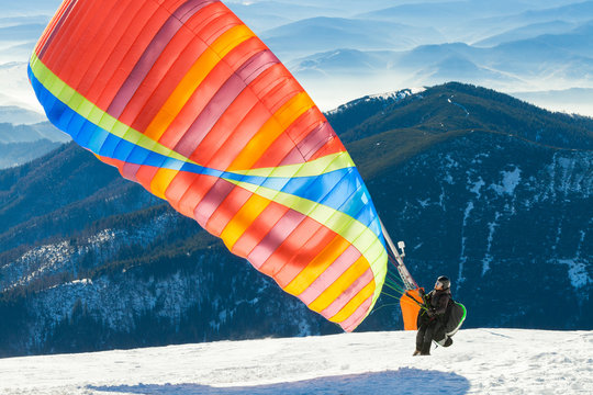 Paraglider launching into air from the very top of a snowy mountain slope