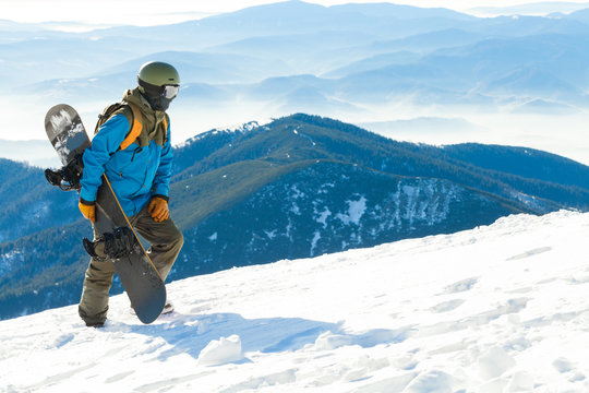 Young snowboarder in helmet walking at the top of a mountain