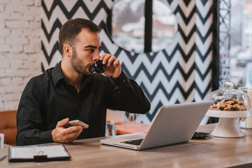 Confident young man working on laptop and drinking coffee while