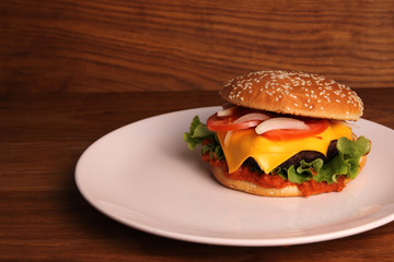 Homemade hamburger with double cheese, tomatoes, onions and on a wooden table  in a white plate, unhealthy food. 