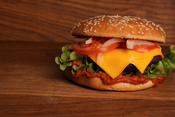 Homemade hamburger with double cheese, tomatoes, onions and on a wooden table, unhealthy food. 