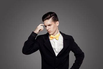 Young trendy man. Black suite, yellow bowtie, gray background. Portrait