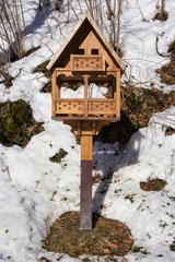 Shelter for tit and bird in winter, birdhouse covered snow and snowflakes in forest, wintertime in garden, trees and birdhouse hanging on the branch. 