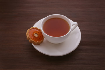 Cup of tea on the table. On a brown background of a white Cup with a saucer. On the plate of 

cookies in the shape of the sun. The drink is brown in a white Cup