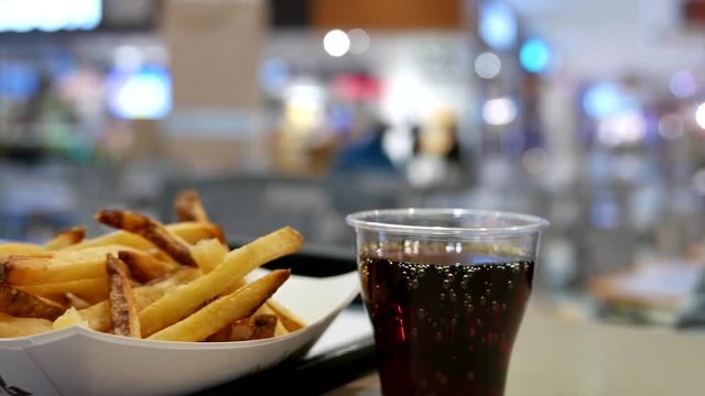 A cup of coke and fries on table at food court inside shopping mall