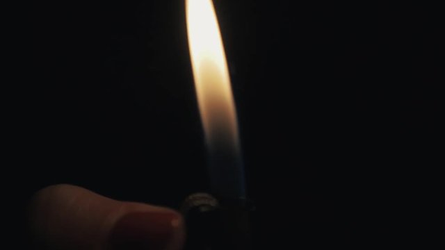 Slowmotion close up woman hand with red nail polish flaming up a lighter in darkness