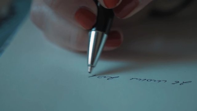 Close up slowmotion female hand with red nail polish writing cursive with ball pen on plain white paper