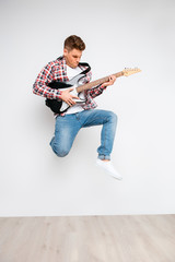 Portrait of trendy rocker guy jumping with electric guitar