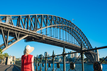 Woman in bright top and hat against Sydney Harbour Bridge on the