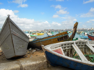 Weathered boats painted with colorful patterns parked at the edge of the sea in Alexandria, Egypt.