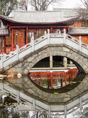 A traditional Chinese bridge reflects in a calm pond in a memorial park in the old city of Dali...