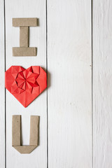 Red origami heart, craft paper folded letters I Love You (I, U) inscription on white painted rustic rural barn wood background. Empty space for copy, text, lettering.