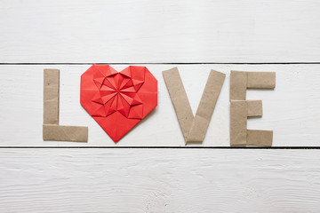 Red origami heart, craft paper folded letters Love inscription on white painted rustic rural barn wood background. Nice Valentines day holiday greeting card, postcard.