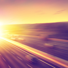 Cars in motion blur on highway during sunset.