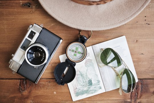Planning next trip on table whith passport, vintage camera, compass, sunglasses and hat.