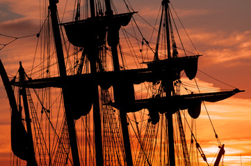 Tall ship masts and rigging silhouetted against a dramatic sky at sunset