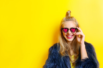 Young beautiful woman wearing sunglasses with hearts on yellow background