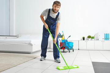 Funny young man moping floor at home