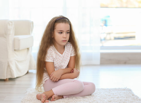 Sad little girl sitting on floor in room