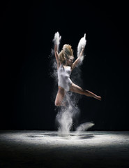 Graceful woman jumping in cloud of white dust