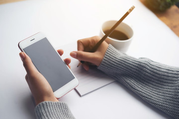 Female hand writing down on letter paper with cup of tea on the wood desk, top view