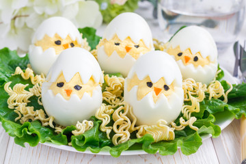 Little chicken in nest, deviled eggs served with salad and dry ramen on white plate, horizontal