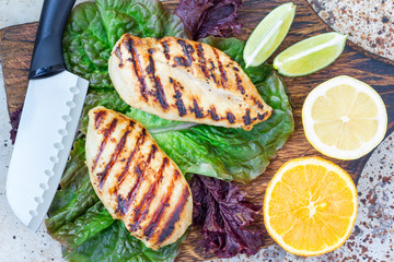 Grilled chicken breast in citrus marinade on salad leaves and wooden cutting board, horizontal, top view