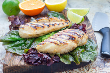 Grilled chicken breast in citrus marinade on salad leaves and wooden cutting board, horizontal