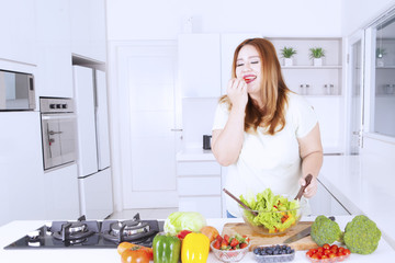 Fat woman tasting salad on the kitchen