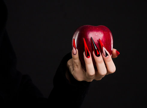 Hands with scary nails manicure holding red apple , isolated on black background