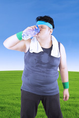 Obese man is drinking in the meadow