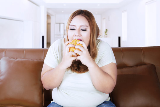 Obese woman with delicious cheeseburger at home