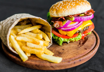 Burger and french fries on a wooden table against black background. Selective focus