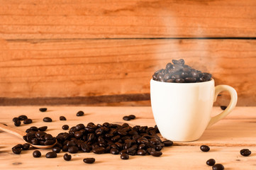 the coffee beans and cup of coffee with smoke on wooden table background