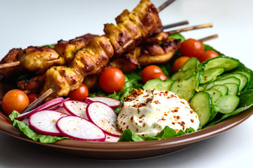 Chicken kebab with vegetables on a clay plate