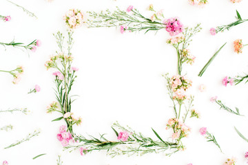 Obraz na płótnie Canvas Wreath frame made of pink and beige wildflowers, green leaves, branches on white background. Flat lay, top view. Valentine's background