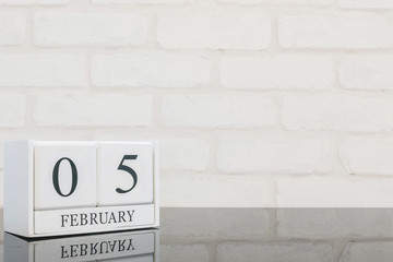 Closeup white wooden calendar with black 5 february word on black glass table and white brick wall textured background with copy space in selective focus at the calendar