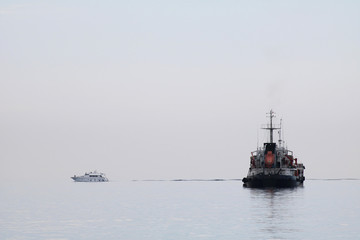 A small boat and big ship on calm sea water in fog
